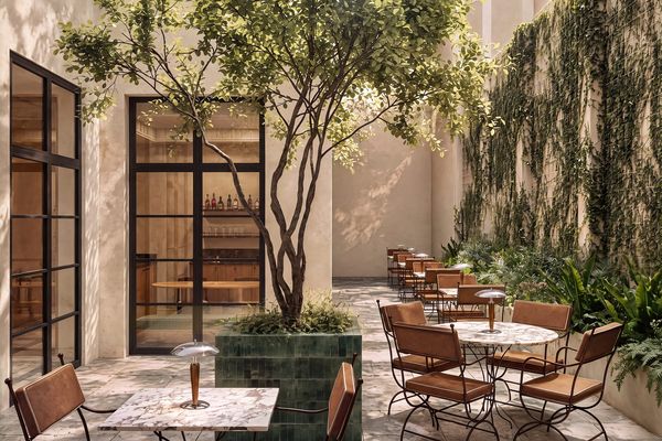 Patio interior ajardinado con árboles, muros vegetales y mesas de terraza